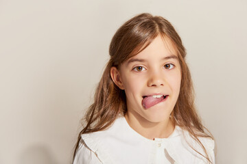 Close up portrait of one little charming girl with long hair grimacing and looking at camera over light background