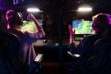 Two male gamers celebrating victory while playing video game on tournament in cybersport club
