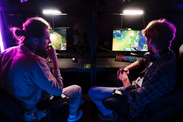 Male friends discussing game strategy while playing video game in cybersport club