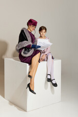 Young beautiful woman and little girl, mother and daughter in retro style clothes sitting on huge box isolated over light background
