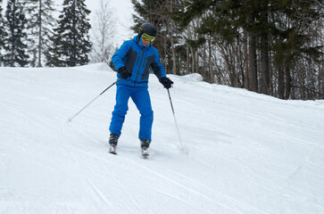 Fototapeta na wymiar A man in blue sportswear on skis rides down a snowy slope
