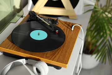 Stylish turntable with vinyl disc and headphones on white chest of drawers at home