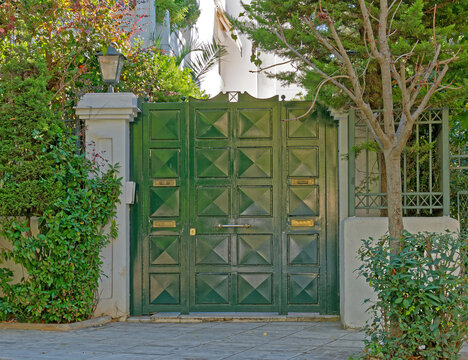 An elegant apartment building entrance with a green painted iron door by the sidewalk. Athens, Greece.