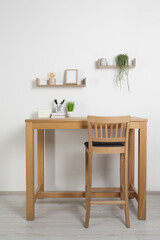 Comfortable workplace with wooden desk near white wall at home
