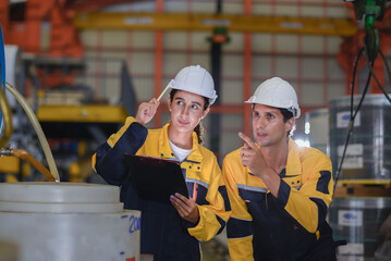 two young engineer assistant in helmet inspection check heavy machine construction installation  industrial metal roof roll sheet factory. colleague friend worker point finger check operation factory