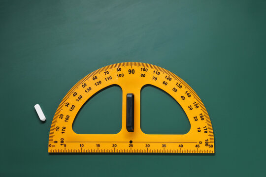 Yellow protractor and chalk on green chalkboard, flat lay. Space for text