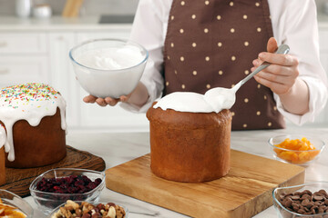 Woman decorating traditional Easter cake with glaze at white marble table in kitchen, closeup