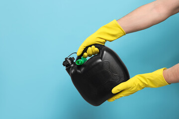 Man in rubber gloves holding black canister on light blue background, closeup. Space for text