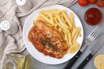 Tasty soda water battered fish, potato chips and lemon slice served on light grey table, flat lay