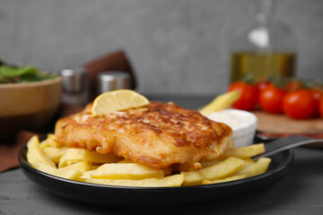 Tasty soda water battered fish, lemon slice and potato chips on dark wooden table