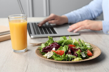Office employee working with laptop at white wooden table, focus on fresh vegetable salad with...