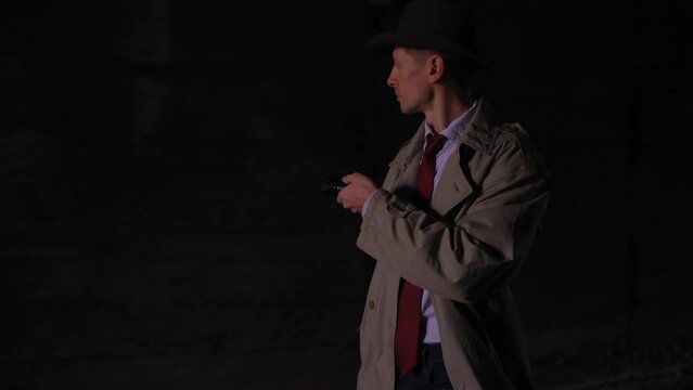 walking around looking around searching detective in a raincoat and hat with a flashlight looking for clues or retro style 1950 dark shot