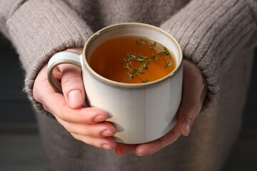 Woman holding cup of tasty herbal tea with thyme, closeup