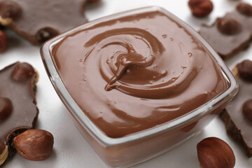 Bowl with tasty paste, chocolate pieces and nuts on white table, closeup