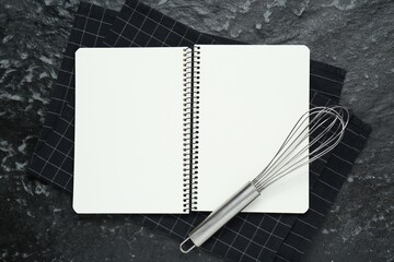 Blank recipe book and whisk on black textured table, flat lay. Space for text