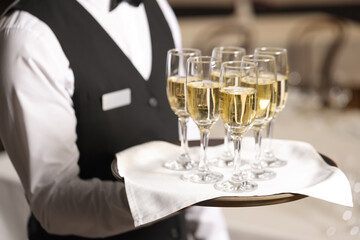 Butler holding tray with glasses of sparkling wine in restaurant, closeup
