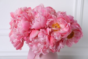Beautiful bouquet of pink peonies in vase near white wall, closeup