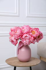 Beautiful bouquet of pink peonies in vase on wooden table indoors