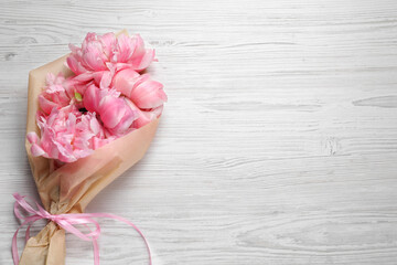 Beautiful bouquet of pink peonies wrapped in paper on white wooden table, top view. Space for text