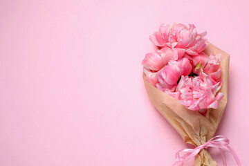 Beautiful bouquet of peonies wrapped in paper on pink background, top view. Space for text