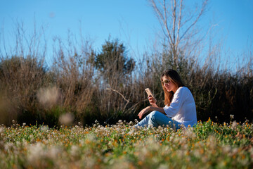 Woman checking her mobile, sitting in a field of flowers.