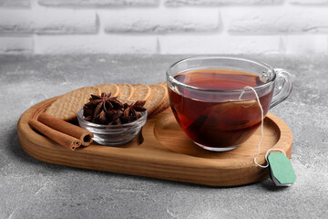 Tea bag in glass cup, anise stars, cinnamon sticks and cookies on light grey table