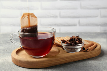 Tea bag in glass cup, anise stars and cinnamon sticks on light grey table