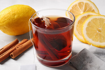 Tea bags, glass of hot drink, cinnamon sticks and lemons on white wooden table, closeup