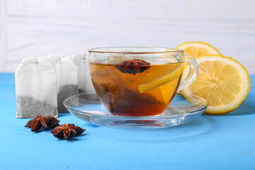 Tea bags, cup of hot drink, anise stars and lemon on light blue wooden table