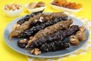 Plate with delicious churchkhelas, nuts and dried fruits on yellow background, closeup