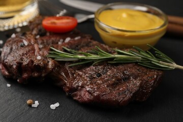 Delicious fried steak with rosemary and sauce on black table, closeup