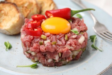 Tasty beef steak tartare served with yolk and other accompaniments on plate, closeup