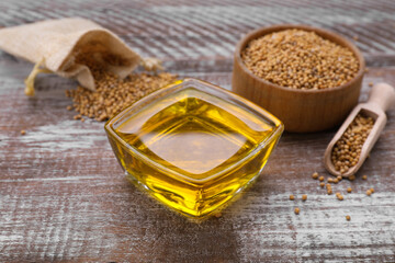 Bowl with natural oil and mustard seeds on wooden table