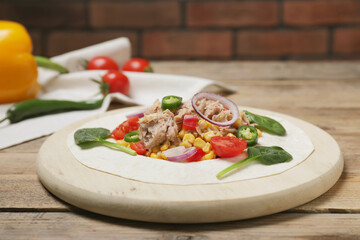 Delicious tortilla with tuna and vegetables on wooden table. Cooking shawarma