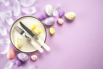 Festive Easter table setting with painted eggs and flowers on purple background. Happy Easter holiday concept