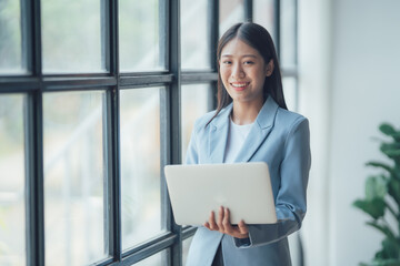 Asian businesswoman talking on phone, using laptop, looking at screen, entrepreneur manager consulting client by call, looking at computer screen, discussing