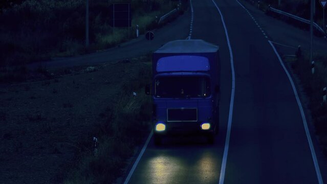 White delivery truck on asphalt road along the green fields in the evening, aerial view. Cargo and delivery concept