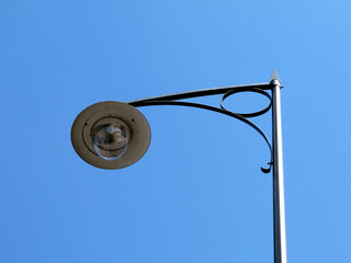 low angle view of retro style lamppost head. closeup detail. glass lens and shiny white reflective lamp hood. clear blue sky.