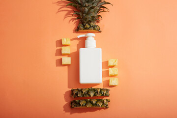 A pump bottle dispenser in white decorated on pastel background with pineapple sliced. Unbranded...