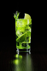Green tarragon lemonade with lime slices in a tall glass with ice on a black background.