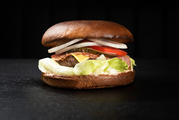 Juicy potato bun cheeseburger on a black background with ham, beef cutlet, greens and vegetables