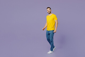 Full body side view young smiling fun confident caucasian man wear yellow t-shirt walking going looking camera isolated on plain pastel light purple color background studio portrait Lifestyle concept