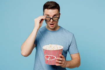 Young shocked surprised amazed impressed man lower 3d glasses wear casual t-shirt watch movie film hold bucket of popcorn in cinema look camera with opened mouth isolated on yellow background studio. © ViDi Studio