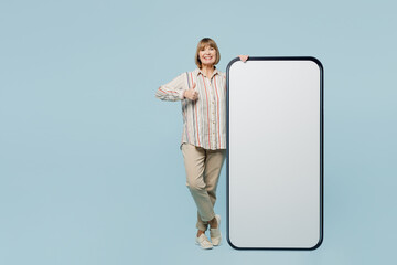 Full body fun elderly woman 50s years old wears shirt big huge blank screen mobile cell phone smartphone with area show thumb up isolated on plain pastel light blue color background studio portrait.