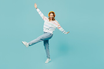 Full body side view smiling young woman wears striped hoody headphones listen to music with...