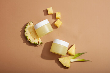 Flat lay of empty label jars arranged on brown background with pineapple slices. Cosmetic product...