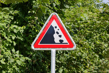 attention falling rocks traffic sign in front of green trees. caution, drive carefully. daytime...