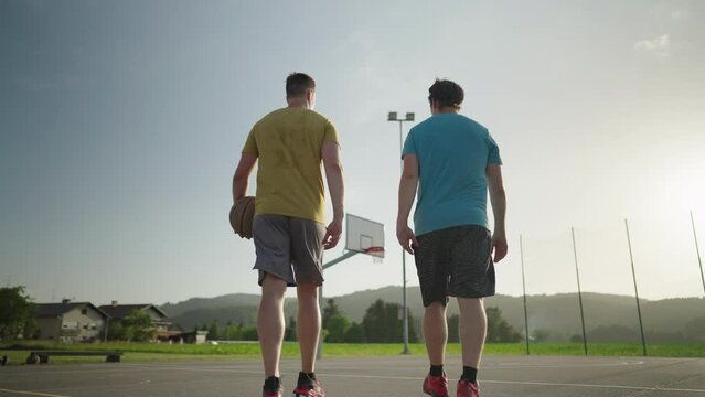 Slow motion - Two male basketball player friends walking towards an outdoor basketball court and giving each other a fist bump. "Game on", "let's go" concept