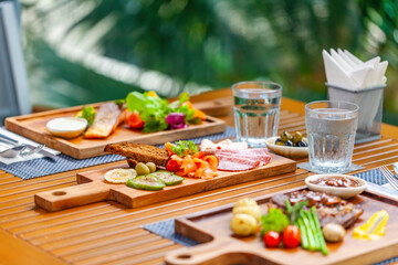 Delicious meat food served on wooden table in outdoor restaurant. Grilled steak, smoked salmon and vegetables, perfect meal on summer day. Healthy and gourmet food selection at luxury hotel.