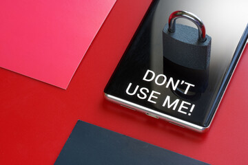 Modern smartphone with the inscription "Don't use me!" and padlock on red and black background. Concept of a ban on the use of a smartphone, cellular communication and gadgets.